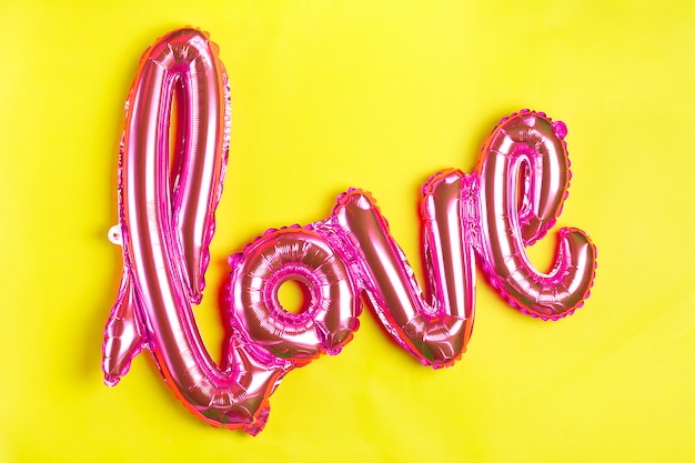 inflatable letters love in coral color on yellow background Flat lay Top view  