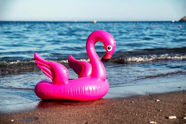 Inflatable pink flamingo on sandy beach with sea at background