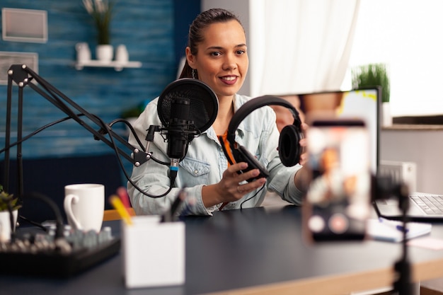 Influencer presenting headphones for giveaway to camera while making video blog in home studio. Creative content creator influencer recording online internet web podcast gift for audience