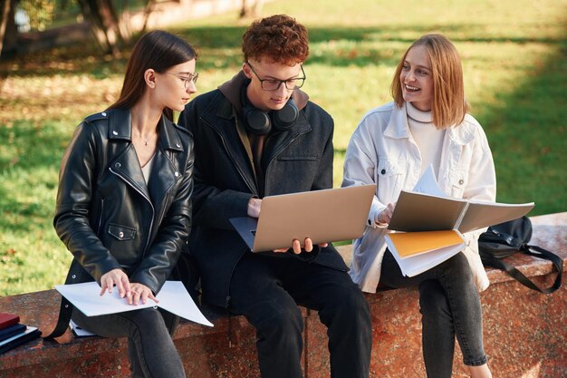 写真 ラップトップで3人の若い学生が大学の外で読んでいる情報