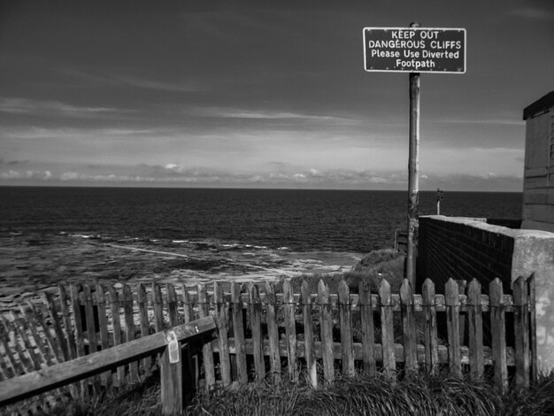 Foto segno informativo con recinzione contro il mare e il cielo nuvoloso