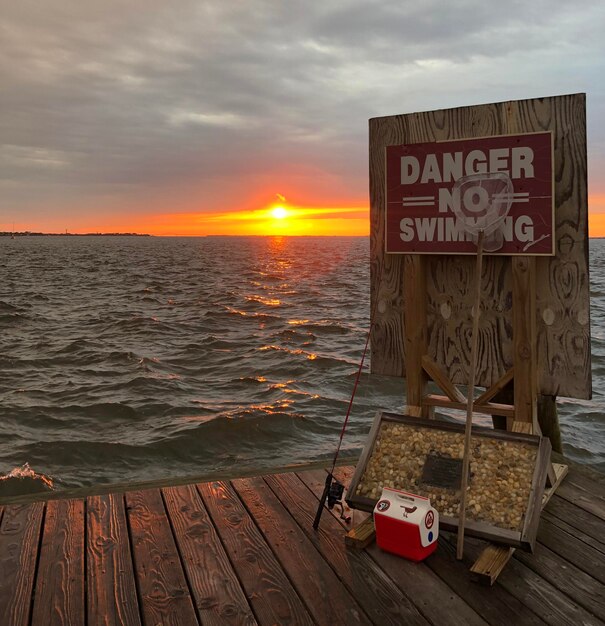 Информационный знак на деревянном столбе на море на фоне неба во время захода солнца