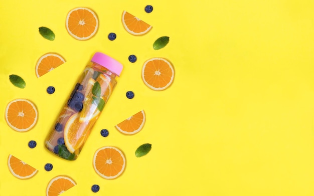 Photo infused or detox water with orange and blueberry in the bottle on the yellow background copy space