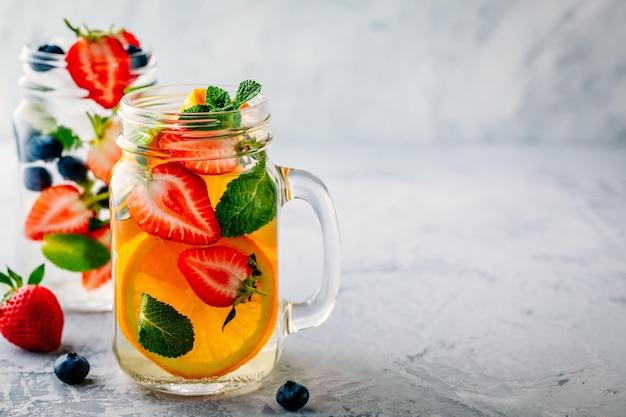 Infused detox water with orange strawberry blueberry and mint Ice cold summer cocktail or lemonade in glass mason jar