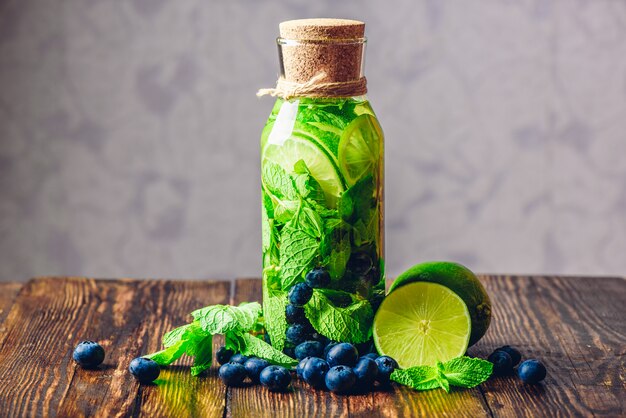 Infused Water in Bottle with Lime, Mint and Blueberry and All Ingredients on Table.