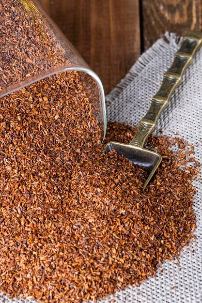 Infuser with dry rooibos leaves on grey wooden table closeup