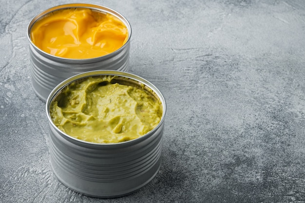 Ingeblikte kaas en guacamole saus in blik, op grijze tafel