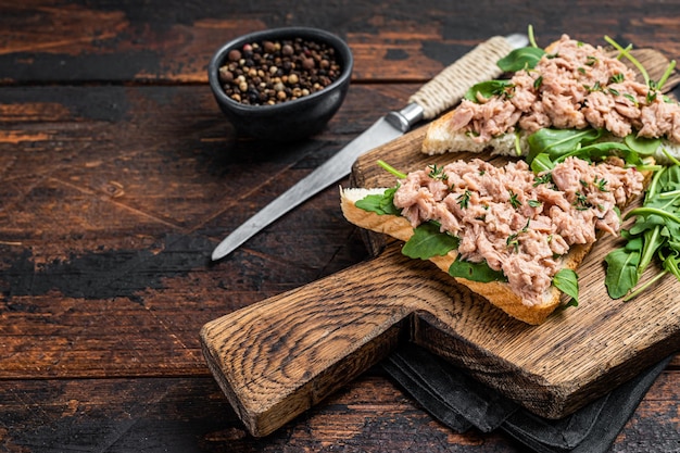 Foto ingeblikte tonijn toast of sandwich met sla en rucola. donkere houten achtergrond. bovenaanzicht. ruimte kopiëren.