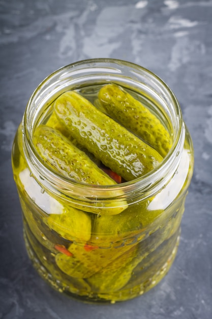 Foto ingelegde augurken of komkommers in glazen pot op een grijze achtergrond