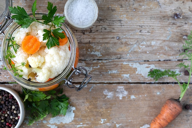 Ingelegde bloemkool met wortelen in een glazen pot op een oude houten tafel. Gefermenteerd voedsel. Kopieer ruimte. bovenaanzicht