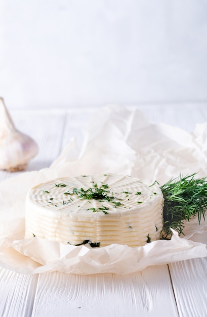 Ingelegde kaas met dille, kruiden en knoflook op een witte houten achtergrond.