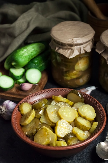 Ingelegde komkommersalade in een kom en potten op zwarte achtergrond