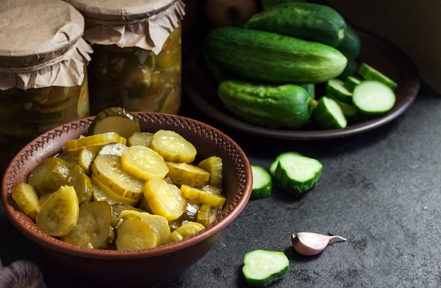 Ingelegde komkommersalade in een kom en potten op zwarte achtergrond