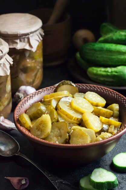 Ingelegde komkommersalade in een kom en potten op zwarte achtergrond