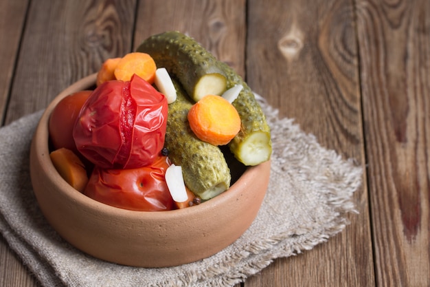 Ingelegde tomaten en komkommers in aardewerk op een houten tafel.