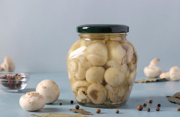 Ingemaakte champignons in een glazen pot op lichtblauwe achtergrond