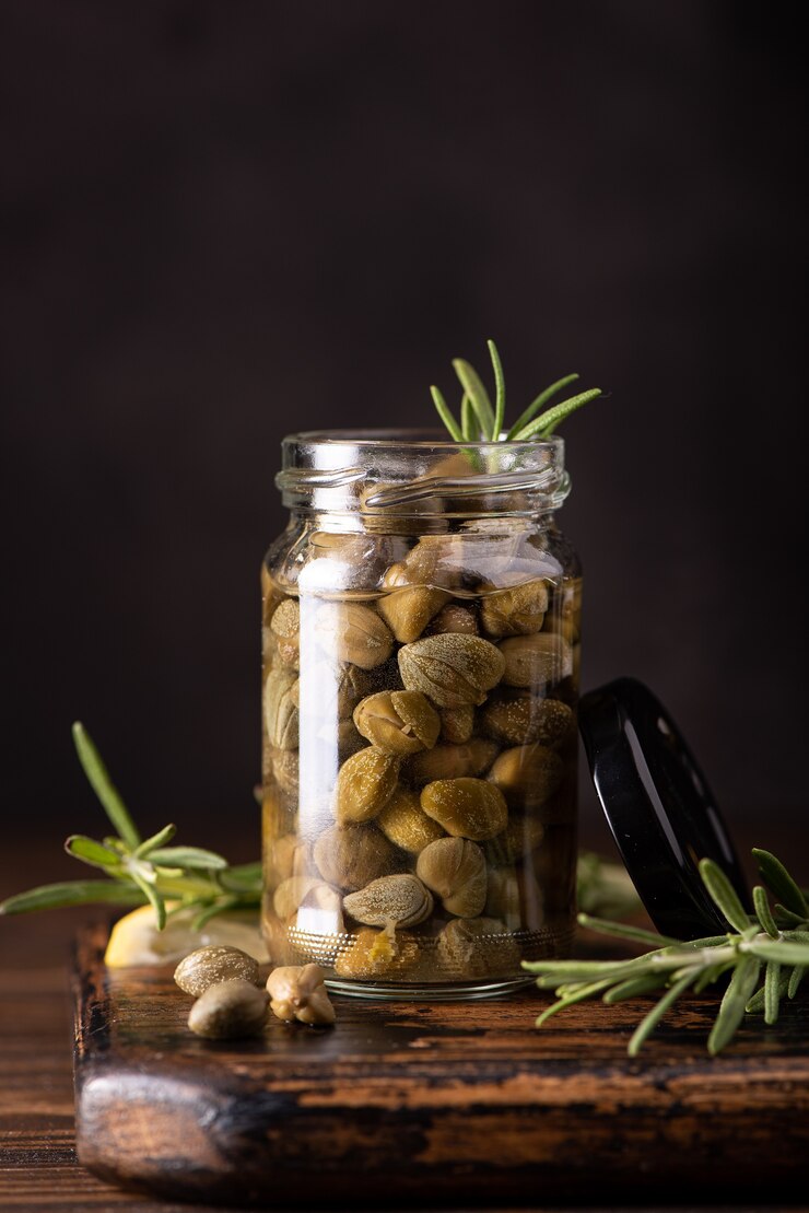 Ingemaakte kappertjes in een glazen pot met kruiden op houten tafel