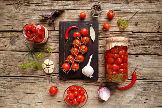 Ingemaakte kerstomaatjes in potten en ingrediënten voor conservering op een oude houten achtergrond