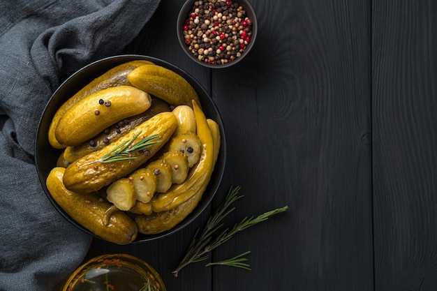 Ingemaakte komkommers met peper en rozemarijn in een kom op een houten ondergrond. Bovenaanzicht, kopieer ruimte.