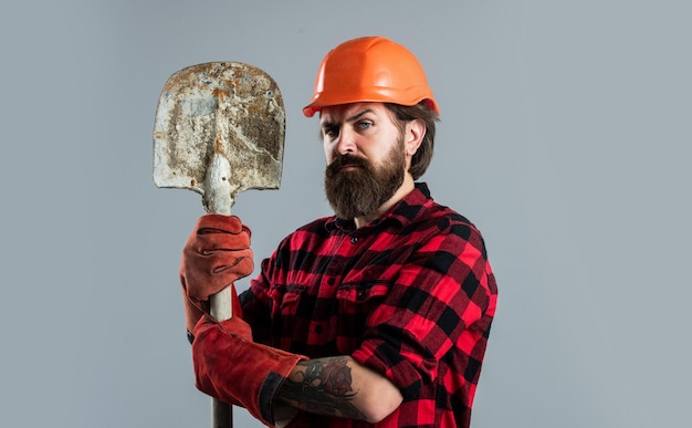 Ingenieur gebruik schop in handschoenen. bouwvakker draag veiligheidshelm. veiligheidsuitrusting dragen. opzichter op de bouwplaats. zelfverzekerde militair. brutale hipster-man. man met harde hoed.