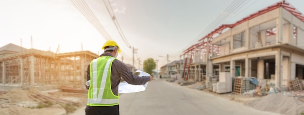 ingenieur in beschermende helm en blauwdrukken op de bouwplaats van het huis