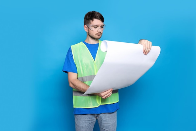 Ingenieur in bril met tekenpapier in handen op blauwe achtergrond