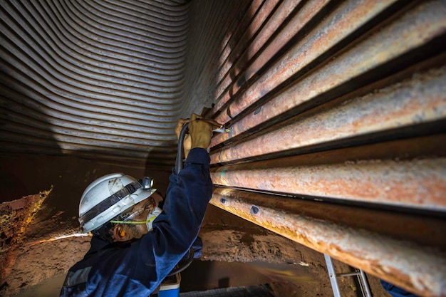 Ingenieur in inspectie en reparatie van gasspiraalverwarmingsapparatuur van stookruimte. Reiniging en onderhoud van staalconstructies van industriële stoomketels in gevaarlijke besloten ruimtes