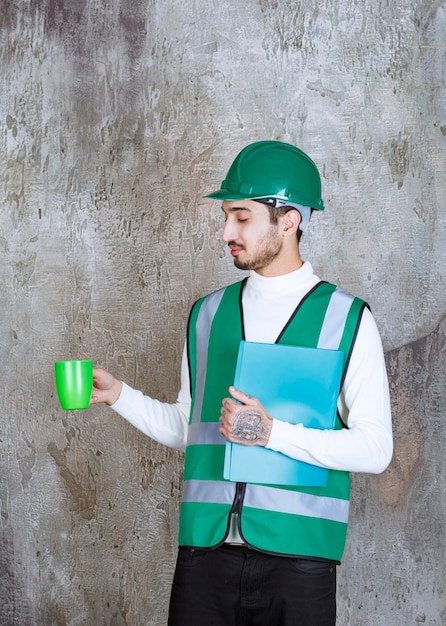 Ingenieur man in geel uniform en helm met een groene koffiemok en een groene map