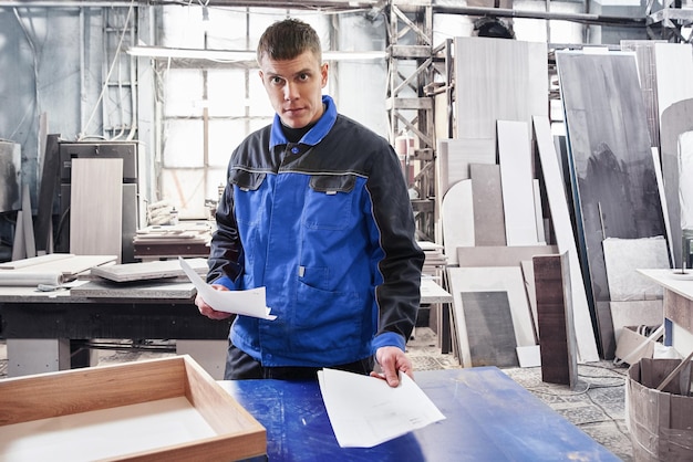 Ingenieur werknemer met tekeningen papieren in handen op de achtergrond van een geautomatiseerde productiefabriek moderne productietechnologieën