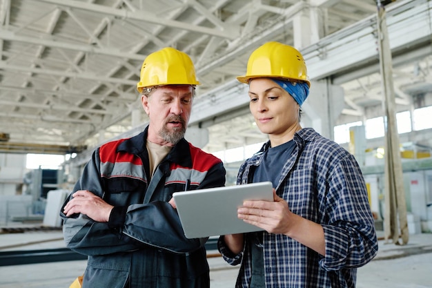 Ingenieurs bespreken online project op tablet-pc terwijl ze in de werkplaats van de fabriek staan