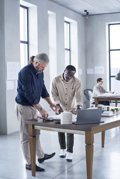 Ingenieurs die aan tafel staan en samen blauwdrukken onderzoeken terwijl ze op een modern kantoor werken