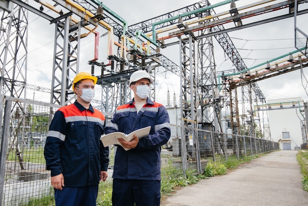 Ingenieurs elektrische onderstations voeren een onderzoek uit van moderne hoogspanningsapparatuur in het masker ten tijde van pandemie. Energie. Industrie.