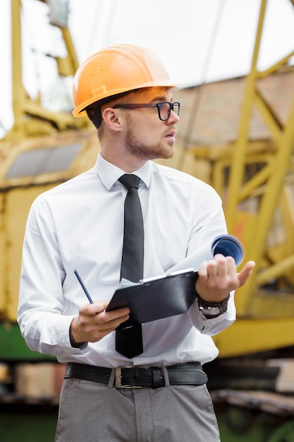 Ingenieursbouwer in een helm houdt tekeningen op de bouwplaats