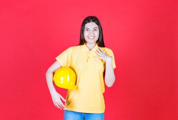 Ingenieursmeisje in gele dresscode die een gele veiligheidshelm vasthoudt en zich positief en gelukkig voelt.