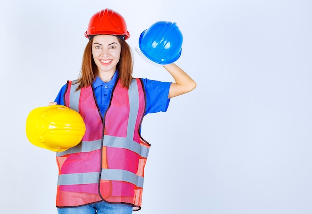 Ingenieursmeisje in uniform dat blauwe en gele helmen vasthoudt en een keuze maakt.