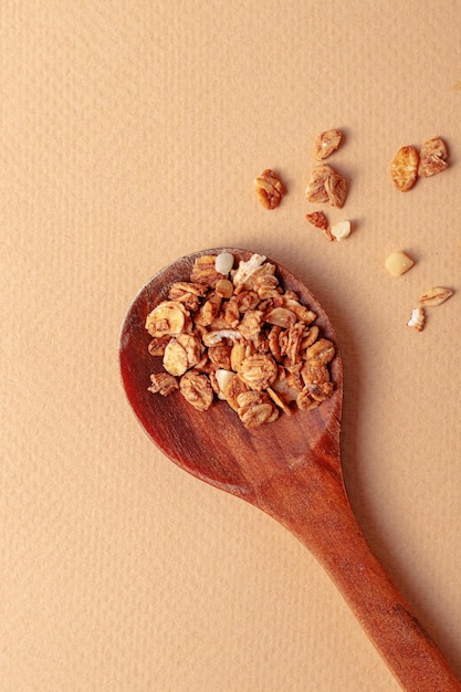 Ingrediente per la colazione granola al forno con cucchiaio di legno su sfondo beige primo piano vista dall'alto