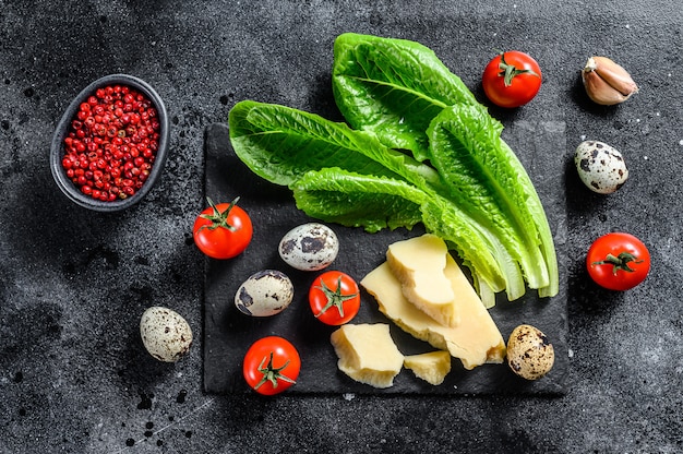 Ingrediënten Caesar salade, Romaine sla, kerstomaatjes, eieren, Parmezaanse kaas, knoflook, peper. Zwarte achtergrond. Bovenaanzicht