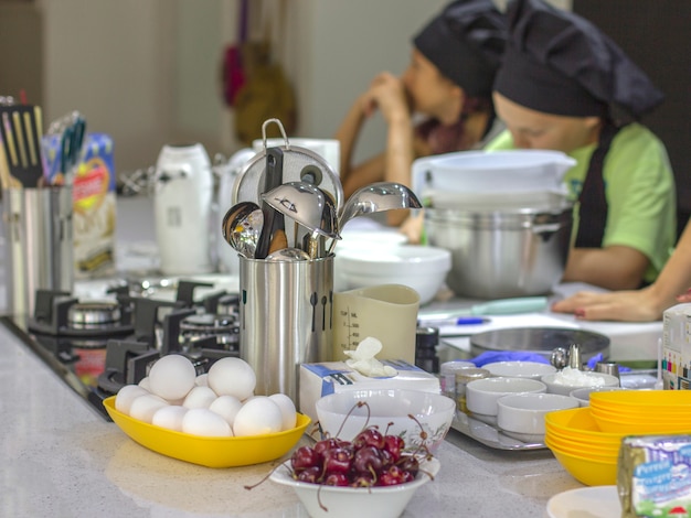 Ingrediënten en kookgerei op de tafel. Kinderen-koks op de achtergrond.