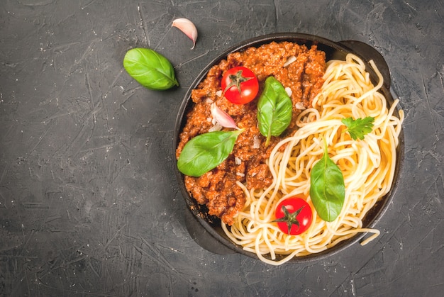 Ingrediënten uit de Italiaanse keuken. Producten voor de bereiding van pasta bolognese, het kookproces. Spaghetti, bolognesesaus, basilicum, knoflook, tomaat, parmezaanse kaas in pan.