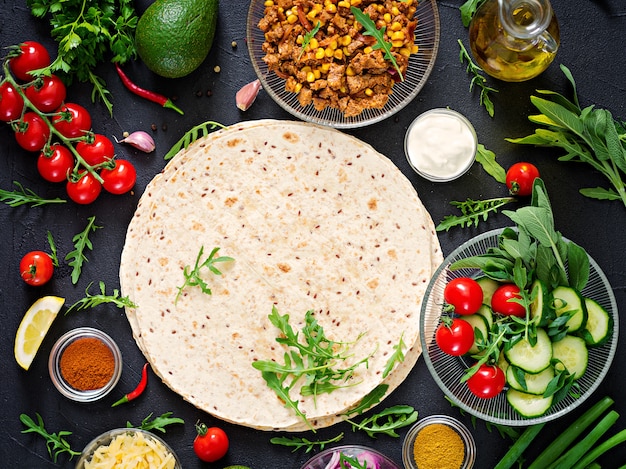 Ingrediënten voor burrito&#39;s wraps met rundvlees en groenten op zwarte achtergrond. Bovenaanzicht