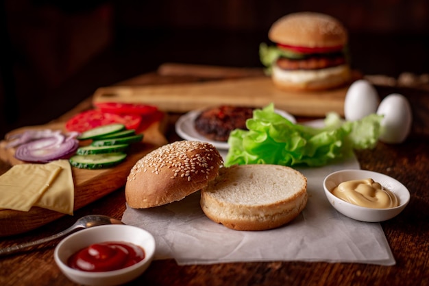 Ingrediënten voor een klassieke hamburger Gegrild vlees groenten Groenten sauzen in de buurt van een sesambroodje Houten achtergrond Koken hamburger of cheeseburger