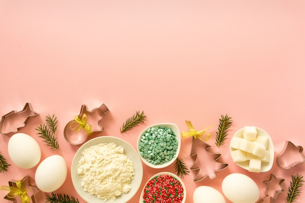 Ingrediënten voor het bakken van kerstkoekjes. eieren, bloem, suiker en zoete hagelslag op een roze achtergrond met kopie ruimte.