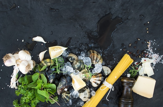 Ingrediënten voor het koken Spaghetti vongole. Tweekleppige schelpdieren op afgebroken ijs, rauwe pasta, Parmezaanse kaas, knoflook, peterselie en citroen over steen