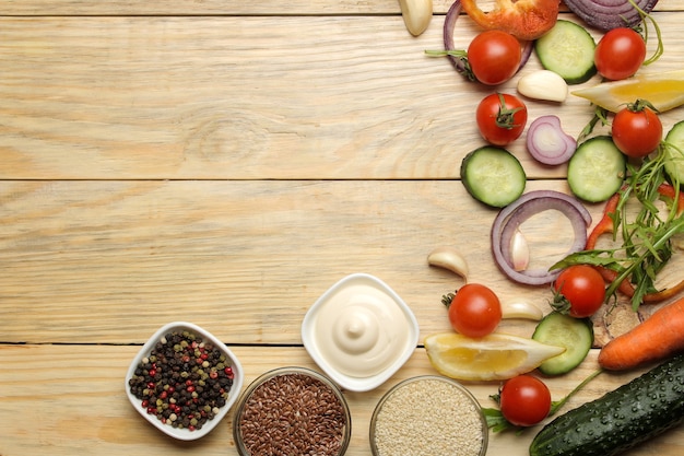 Ingrediënten voor het koken van salade. diverse groenten en kruiden wortelen, tomaten, uien, komkommers, paprika's en rucola op een natuurlijke houten tafel. bovenaanzicht.