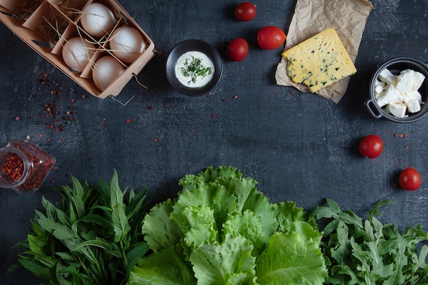 Ingrediënten voor het koken van salade. verse, biologische groenten, eco-eieren en groenten. tomaat en kaas op donkere stenen tafel met kopie ruimte. plat liggen. gezond eten concept