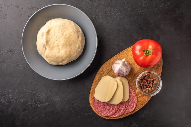 Ingrediënten voor het koken van zelfgemaakte pizza met mozzarella en salami op een donkere achtergrond.