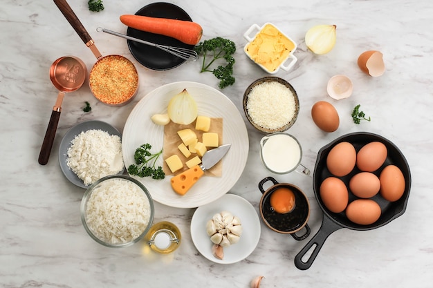 Ingrediënten voor het maken van Arancini koken op een achtergrond van wit grijs marmer. Kaas, Rijst, Melk, Ei, Wortel, Peterselie, Boter, Knoflook, Broodkruim en Parmezaanse kaas