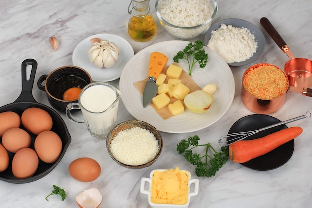 Ingrediënten voor het maken van Arancini koken op een achtergrond van wit grijs marmer. Kaas, Rijst, Melk, Ei, Wortel, Peterselie, Boter, Knoflook, Broodkruim en Parmezaanse kaas