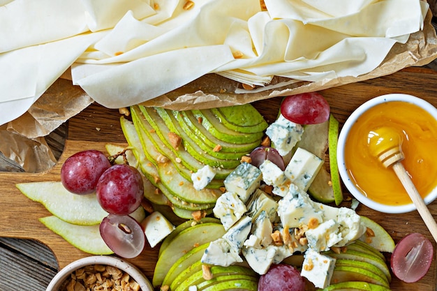 Ingrediënten voor het maken van een filodeegtaart, fruit (druiven, peren), kaas en noten met honing.