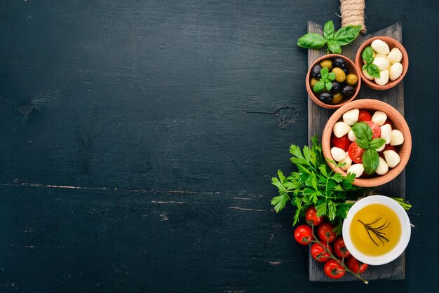 Ingrediënten voor Italiaanse caprese salade Mozzarella kaas cherry tomaten basilicum bladeren olijven olie peper op een zwarte houten achtergrond vrije ruimte voor tekst